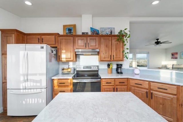 kitchen with light countertops, electric range, brown cabinetry, freestanding refrigerator, and under cabinet range hood