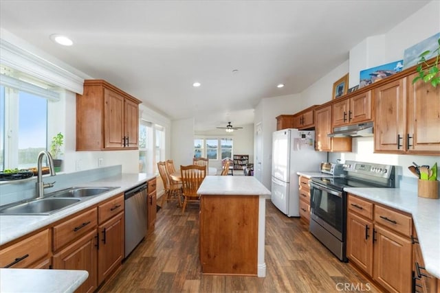 kitchen featuring appliances with stainless steel finishes, a center island, light countertops, under cabinet range hood, and a sink