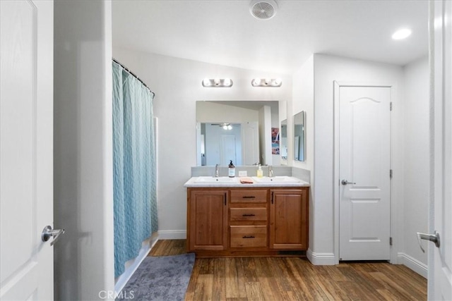 bathroom featuring a shower with shower curtain, a sink, wood finished floors, baseboards, and double vanity