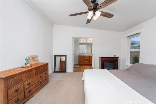 bedroom featuring ensuite bathroom, a ceiling fan, light carpet, a sink, and baseboards