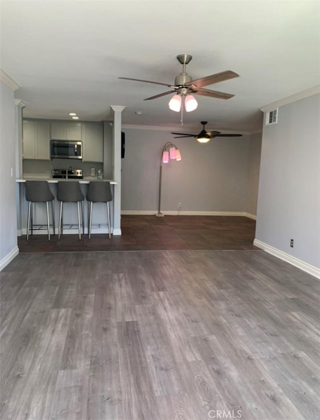 unfurnished living room with visible vents, crown molding, baseboards, and wood finished floors