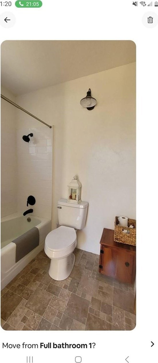 bathroom with stone finish flooring, bathing tub / shower combination, and toilet