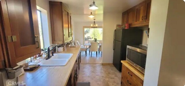 kitchen featuring a sink, light countertops, brown cabinets, stainless steel microwave, and decorative light fixtures