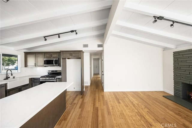 kitchen featuring a fireplace, stainless steel appliances, light countertops, lofted ceiling with beams, and a sink