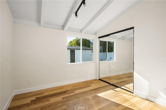 unfurnished room featuring lofted ceiling with beams, track lighting, baseboards, and wood finished floors