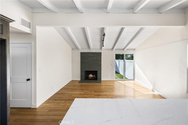 unfurnished living room featuring lofted ceiling with beams, a fireplace, wood finished floors, visible vents, and baseboards