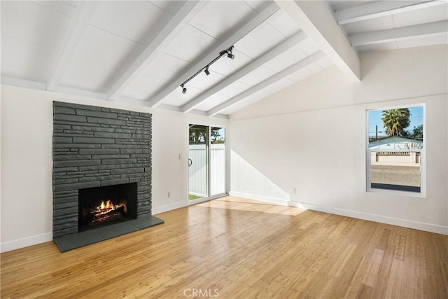 unfurnished living room with lofted ceiling with beams, baseboards, wood finished floors, and a stone fireplace