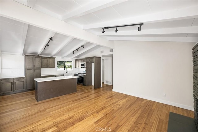 kitchen with lofted ceiling with beams, stainless steel appliances, light countertops, light wood-type flooring, and a center island