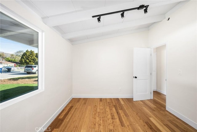 spare room with vaulted ceiling with beams, track lighting, baseboards, and wood finished floors