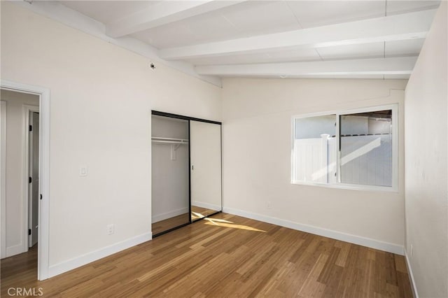 unfurnished bedroom with vaulted ceiling with beams, a closet, baseboards, and wood finished floors