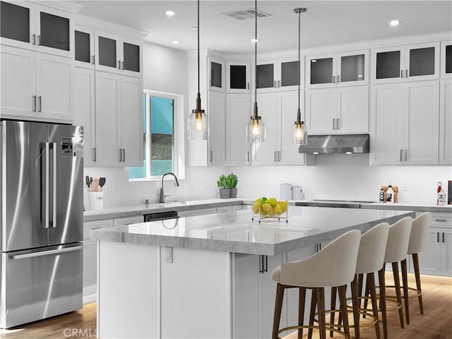 kitchen featuring visible vents, a kitchen island, under cabinet range hood, appliances with stainless steel finishes, and a kitchen bar