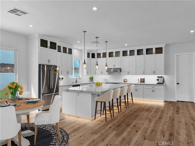 kitchen featuring visible vents, under cabinet range hood, a center island, freestanding refrigerator, and light wood-style floors