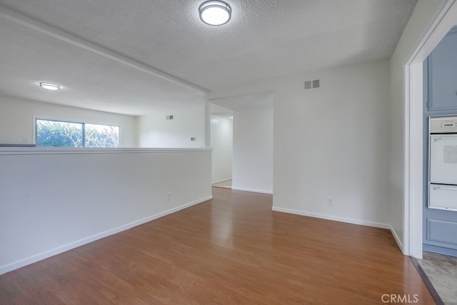 unfurnished room with visible vents, a textured ceiling, baseboards, and wood finished floors