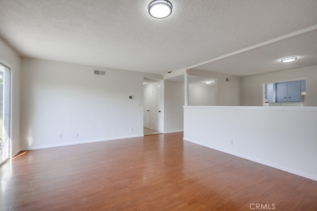 spare room featuring visible vents, a textured ceiling, baseboards, and wood finished floors