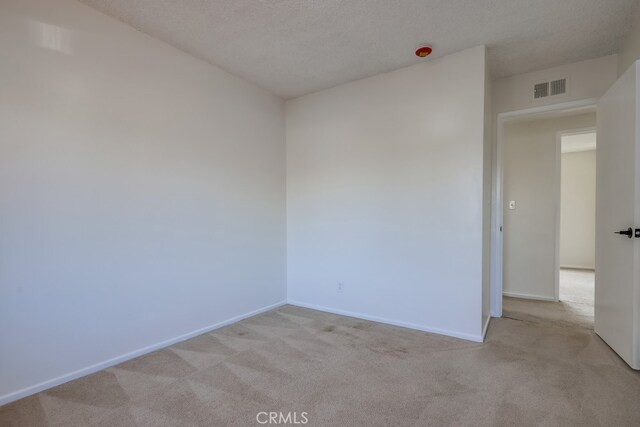 empty room with baseboards, visible vents, a textured ceiling, and light colored carpet