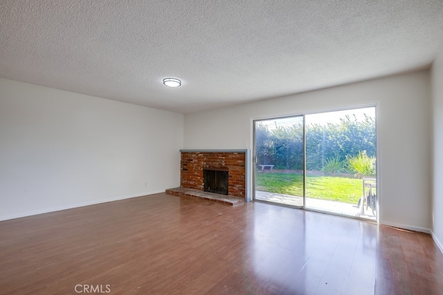 unfurnished living room featuring a brick fireplace, a textured ceiling, baseboards, and wood finished floors