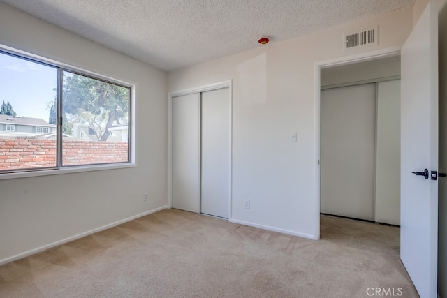 unfurnished bedroom featuring a textured ceiling, light carpet, visible vents, baseboards, and a closet