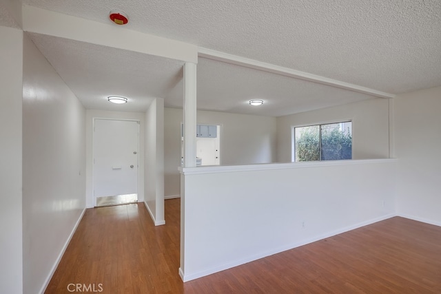 corridor with a textured ceiling, baseboards, and wood finished floors