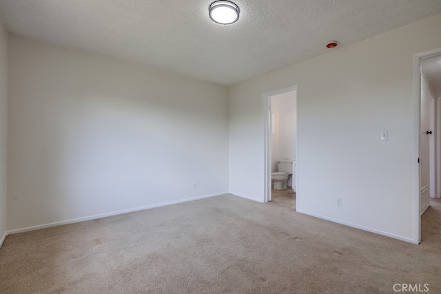 empty room with light carpet, a textured ceiling, and baseboards