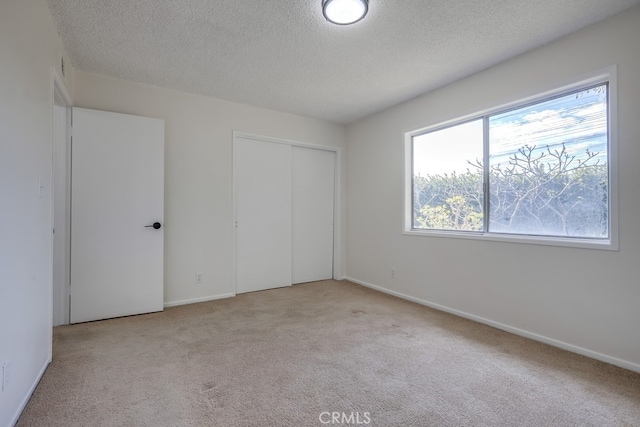 unfurnished bedroom with light carpet, a closet, a textured ceiling, and baseboards