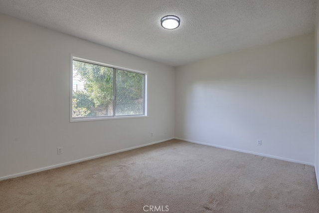 spare room featuring light carpet, baseboards, and a textured ceiling