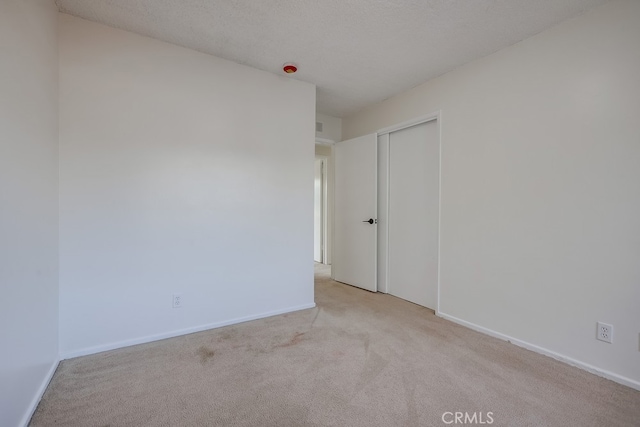 spare room featuring baseboards, a textured ceiling, and light colored carpet