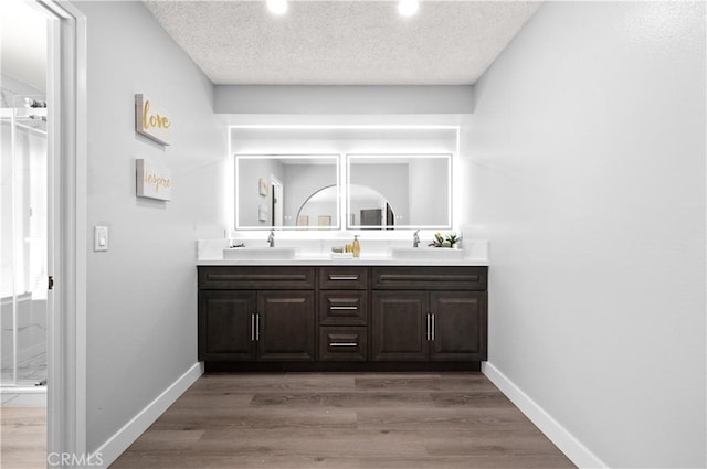 bathroom with double vanity, a sink, a textured ceiling, wood finished floors, and baseboards