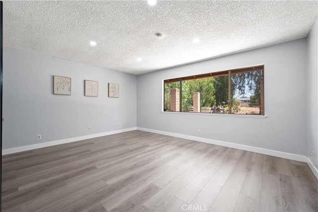 spare room with a textured ceiling, baseboards, and wood finished floors