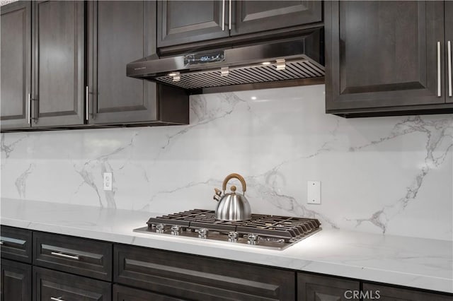 kitchen with tasteful backsplash, light stone countertops, ventilation hood, dark brown cabinets, and stainless steel gas stovetop