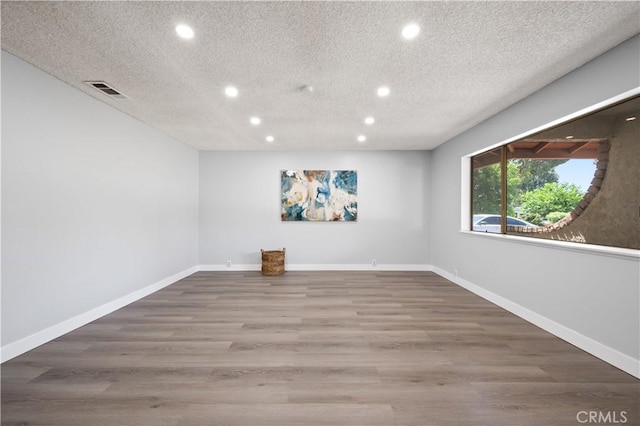 empty room featuring a textured ceiling, recessed lighting, wood finished floors, visible vents, and baseboards