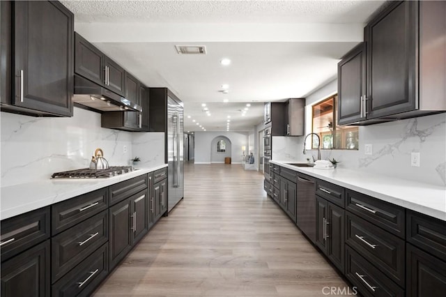 kitchen with range hood, light wood finished floors, light countertops, visible vents, and appliances with stainless steel finishes