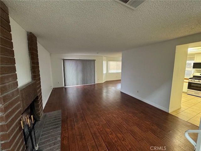 spare room with a textured ceiling, a fireplace, visible vents, and wood finished floors