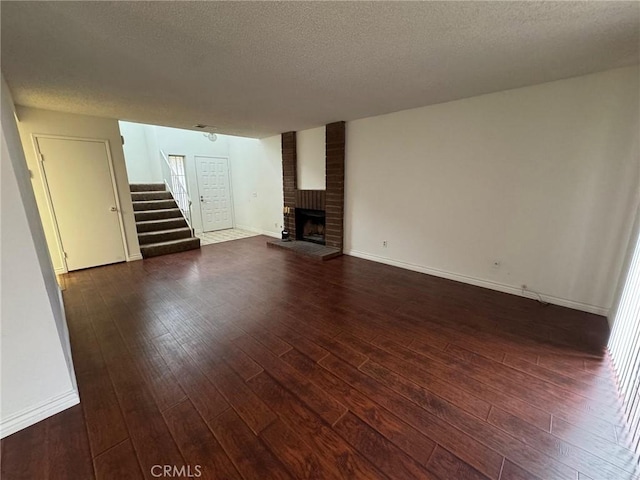 unfurnished living room with baseboards, dark wood-style floors, stairs, a textured ceiling, and a brick fireplace