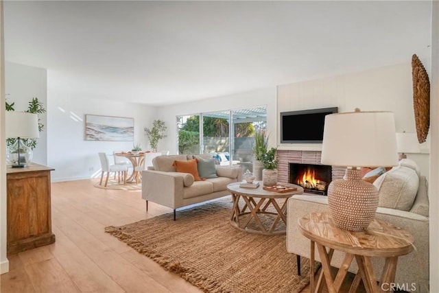 living room with a brick fireplace, light wood-type flooring, and baseboards