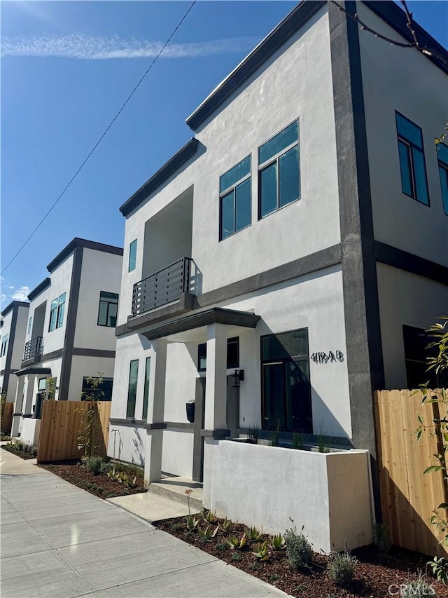 contemporary home with a fenced front yard, a balcony, and stucco siding