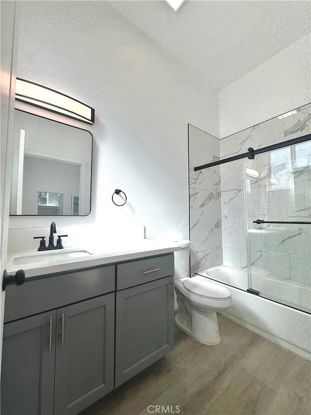 full bathroom featuring bath / shower combo with glass door, vanity, toilet, and wood finished floors