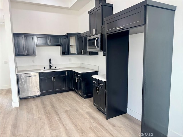 kitchen featuring light wood finished floors, dark cabinets, stainless steel appliances, light countertops, and a sink