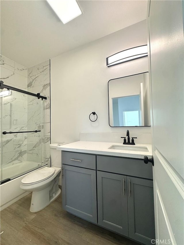 bathroom with shower / bath combination with glass door, vanity, toilet, and wood finished floors