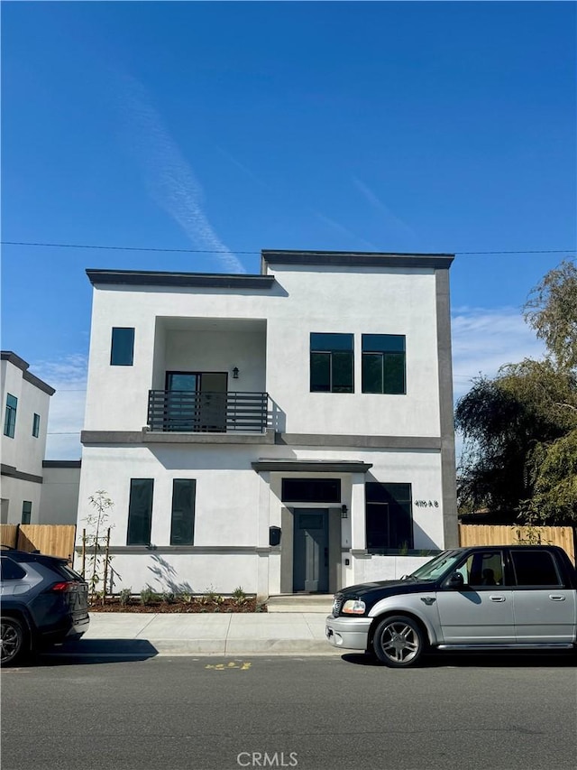 contemporary home featuring fence, a balcony, and stucco siding