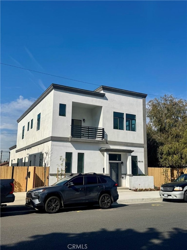 view of front facade with fence, a balcony, and stucco siding