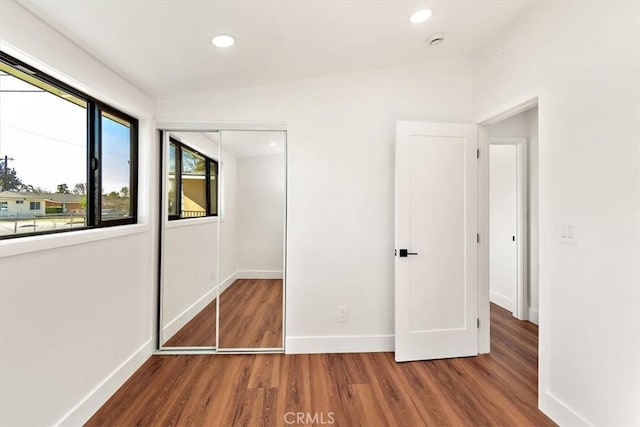 unfurnished bedroom with recessed lighting, a closet, vaulted ceiling, wood finished floors, and baseboards