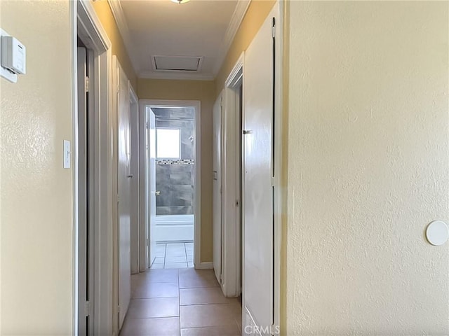 hall with light tile patterned floors, a textured wall, attic access, and crown molding