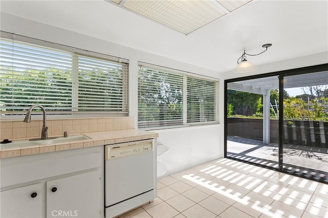 kitchen featuring tile countertops, white dishwasher, a sink, white cabinetry, and a healthy amount of sunlight