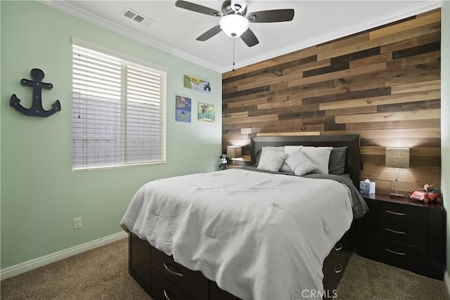 bedroom with wooden walls, visible vents, baseboards, ornamental molding, and dark carpet