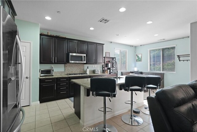 34306 Deergrass Way, Lake Elsinore, CA 92532 - kitchen featuring appliances with stainless steel finishes, decorative backsplash, light tile patterned floors, a kitchen bar, and visible vents