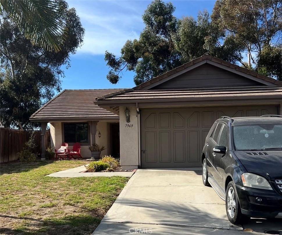 ranch-style house featuring an attached garage, fence, driveway, stucco siding, and a front lawn