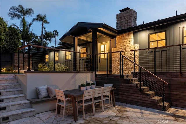 rear view of property with outdoor dining area, stairs, stone siding, a chimney, and a patio area