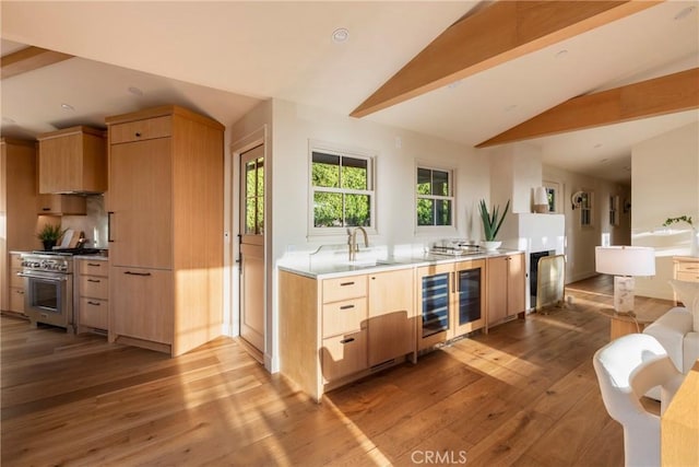 kitchen with beverage cooler, high end range, vaulted ceiling, light countertops, and light brown cabinets