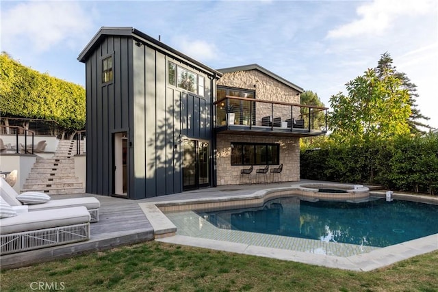 back of house featuring a balcony, a pool with connected hot tub, stone siding, stairway, and board and batten siding