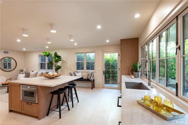 kitchen with a kitchen island, a breakfast bar, oven, a sink, and recessed lighting